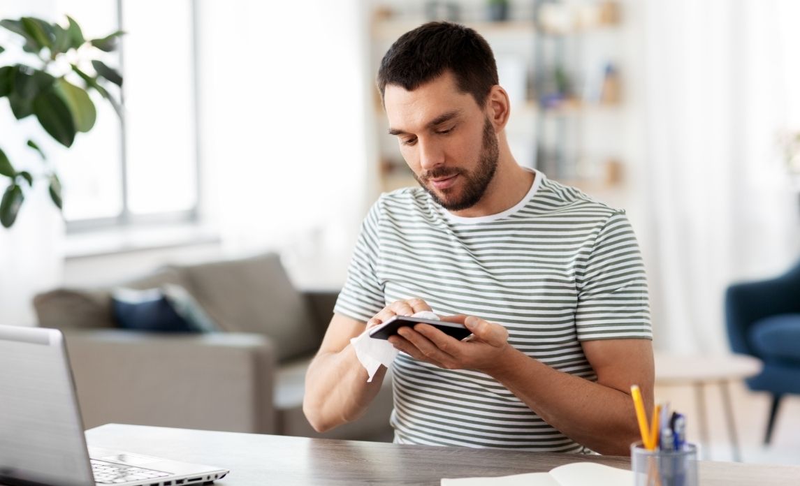 Office worker using disinfectant wipes on his device
